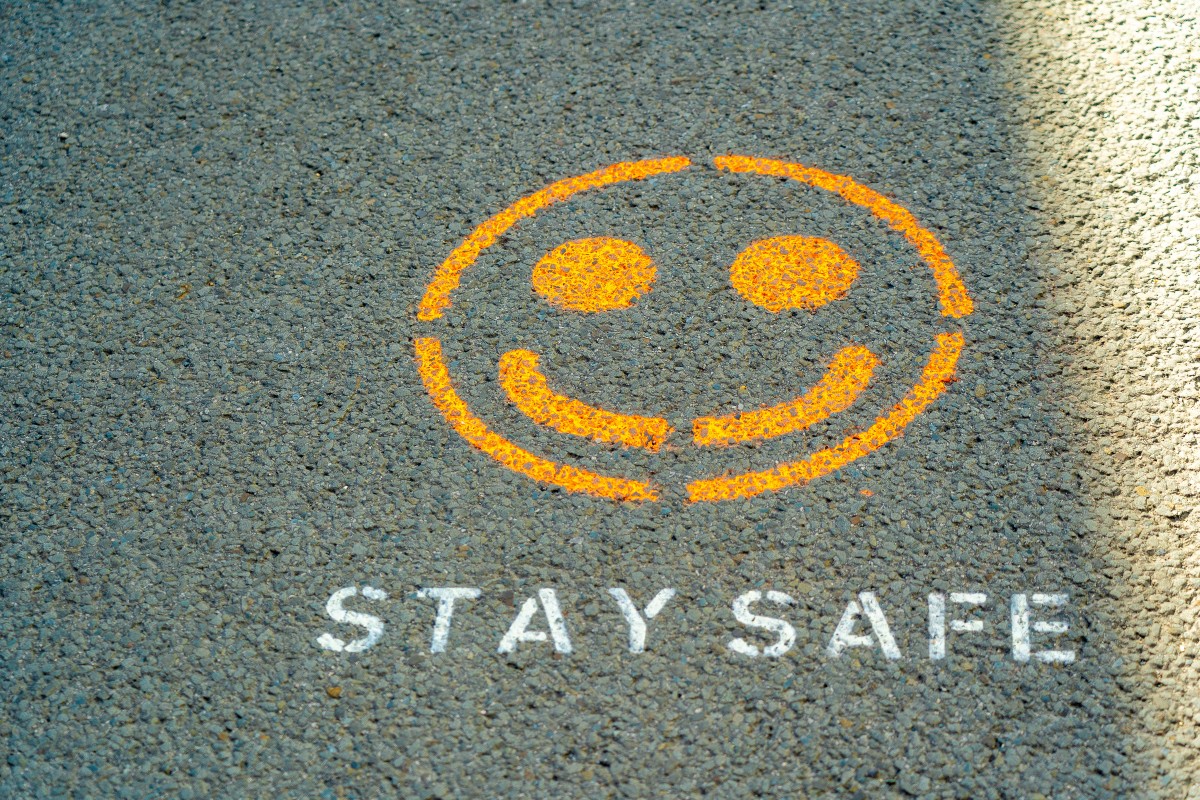 Na betonie namalowana żółtym sprayem uśmiechnięta buźka, pod nią napis białym sprayem STAY SAFE. Ilustracja do postu o zapobieganiu zadławienia u niemowląt.